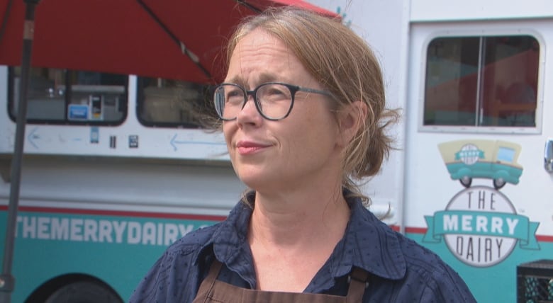 A woman wearing glasses stands in front of a food truck.